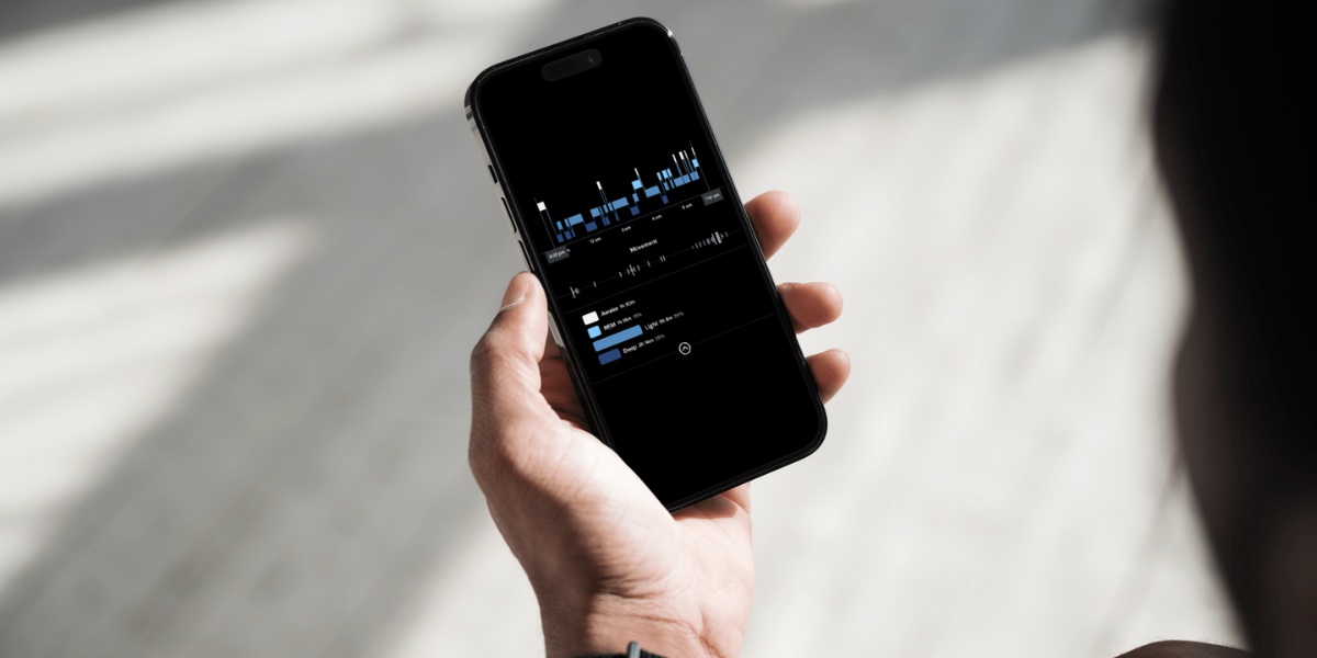 Hand holding a phone with a sleep tracking app on the screen showing sleep patterns