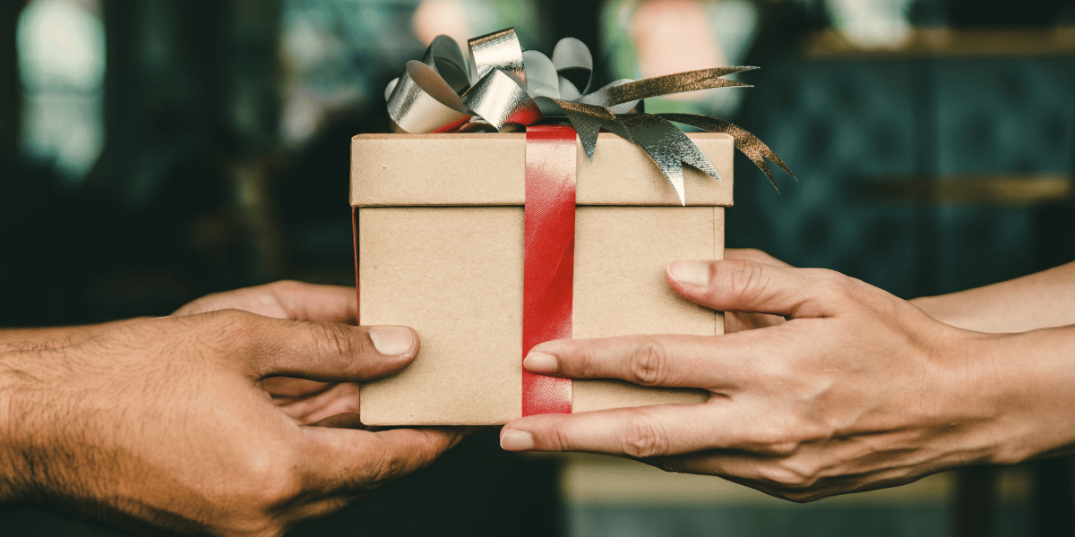 one person hands a gift box with a bow to another person