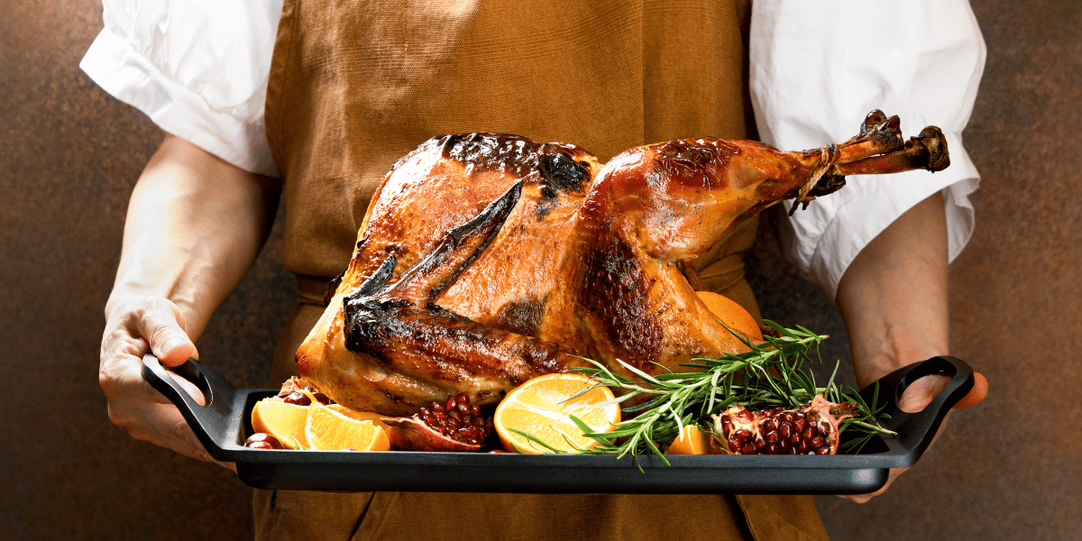 a person in an apron holding a roasted turkey on a platter